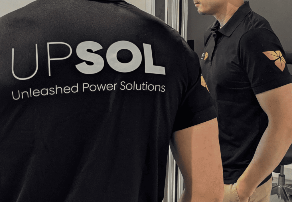 Black custom polo shirts featuring large UPSol screen-printed branding on the back and printed logos on the chest and sleeve.